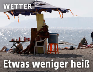 Mann sitzt am Strand unter einem Sonnenschirm