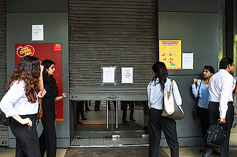 © APA/AFP/Chandan Khanna Inder stehen vor einer geschlossenen McDonalds-Filiale in Neu Delhi
