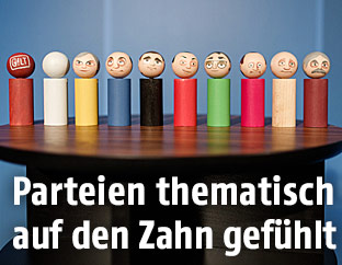Holzfiguren mit Gesichtern der Spitzenkandiaten in den Parteifarben