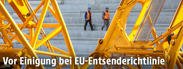 Zwei Bauarbeiter zwischen gelben Kranauslegern