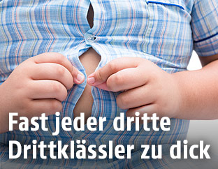 Ein übergewichtiger Bub knöpft sich sein Hemd zu