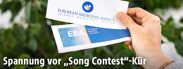 Frau hält die Logos der EU-Agenturen EMA und EBA in die Kamera