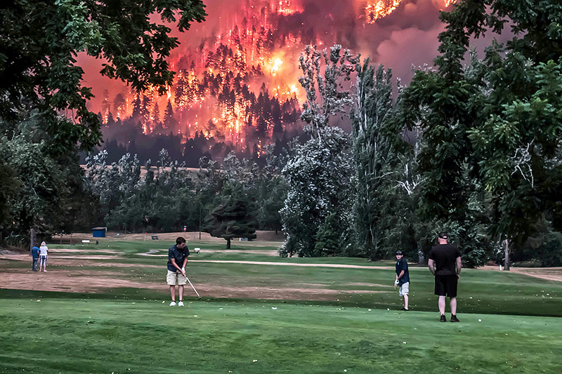 © Reuters/Kirsti McCluer Mehrere Menschen spielen Golf, während im Hintergrund ein Waldbrand tobt