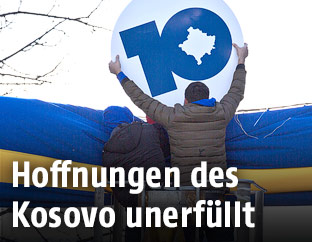 Zwei Männer halten ein Jubiläumsschild anlässlich der 10-Jahres-Feier des Kosovo in die Höhe