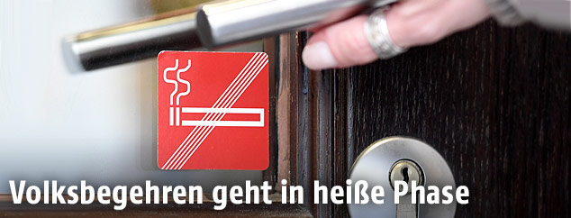 Eine Frau dr&uuml;ckt eine T&uuml;rklinke zu einem Lokal mit Rauchverbot