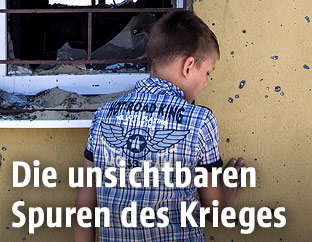Ein Kind vor einer löchrigen Mauer