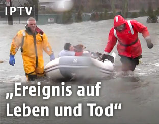 Eine Person wird von zwei Feuerwehrleuten aus den Fluten gerettet