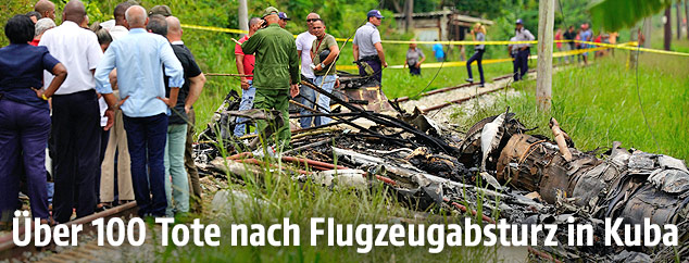 Personen stehen neben Flugzeugwrackteilen
