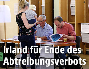 Eine junge Frau mit einem Baby am Arm in einem Wahllokal bei der Abstimmung