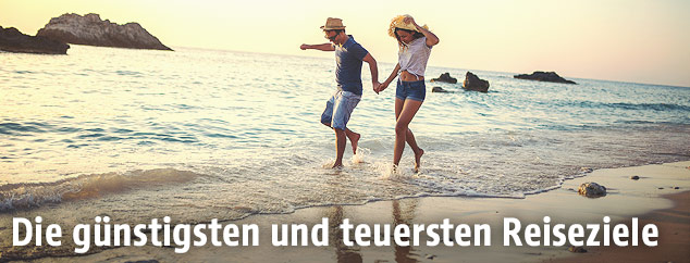 Ein Paar geht im Sonnenuntergang am Strand durchs Wasser