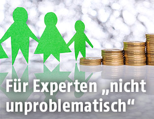 Scherenschnitt einer Familie neben aufgestapelten Münzhaufen