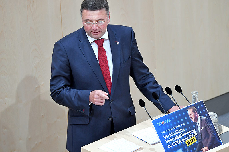 Der Abgeordnete Jörg Leichtfried (SPÖ), vor ihm ein Bild mit der FPÖ-Aufforderung für eine verbindliche Volksabstimmung zu CETA und TTIP